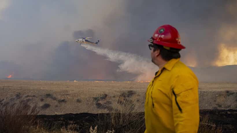 Bombeiros combatendo incêndio florestal com chamas e fumo visíveis ao fundo