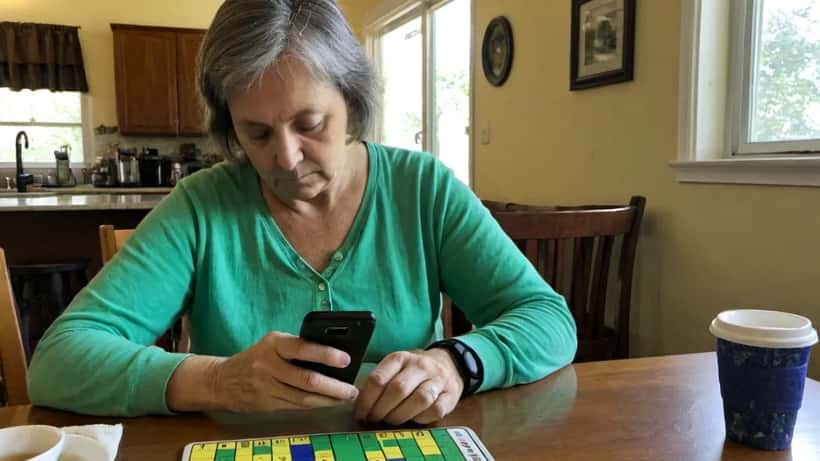 Woman solving the NYT Connections word puzzle on her smartphone at a kitchen table