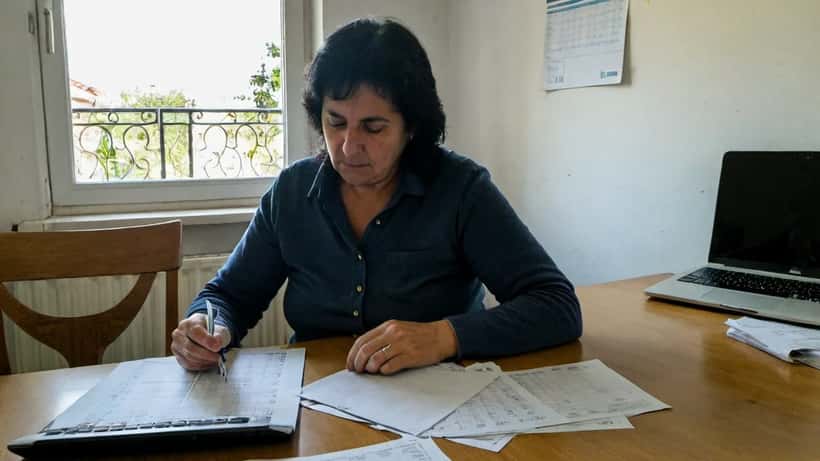 Mulher portuguesa a rever fatura de eletricidade na cozinha com calculadora e contador inteligente ao fundo