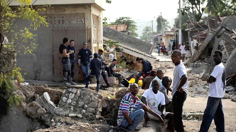 Residentes portugueses avaliando danos em edifício após sismo, com paredes rachadas e detritos