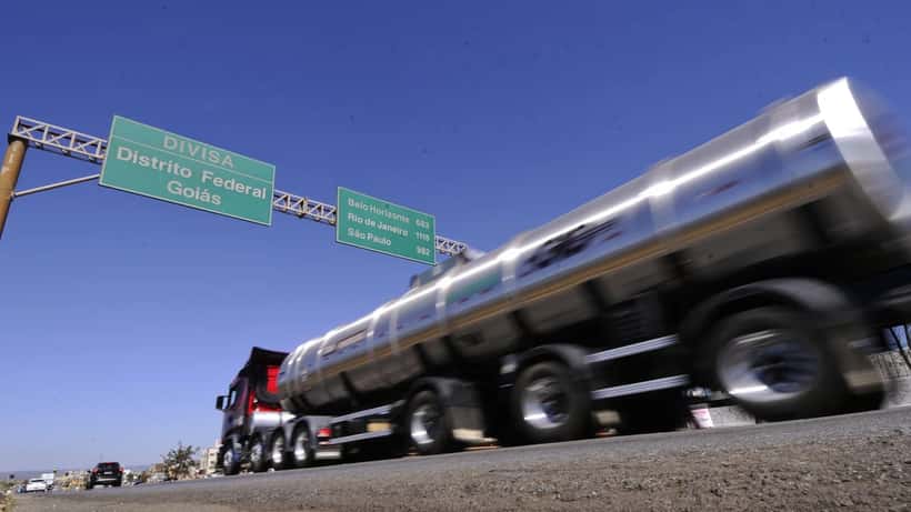 Movimento de caminhões e carros em rodovia federal brasileira com placas de sinalização ao longo da via