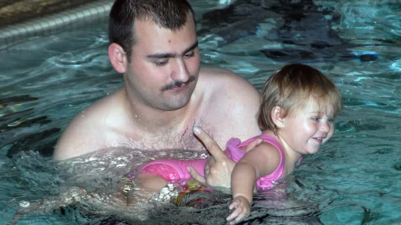 Vater hilft Kind beim Schwimmenlernen – Eltern-Kind-Kurs in österreichischem Hallenbad
