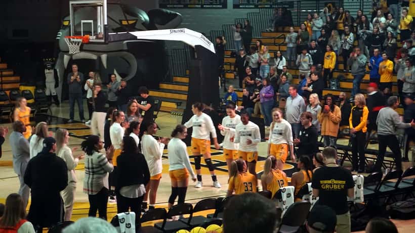 Women basketball players during game introductions at an indoor arena showing team dynamics and athletic readiness