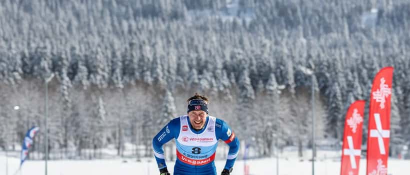 Langrennsløper i mål på Lygna skianlegg i Norge, vinterlandskap med birketrær