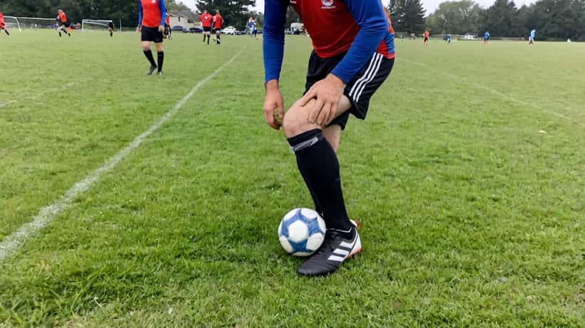 Amateur soccer player holding hamstring in pain on grass field after sprint during recreational match