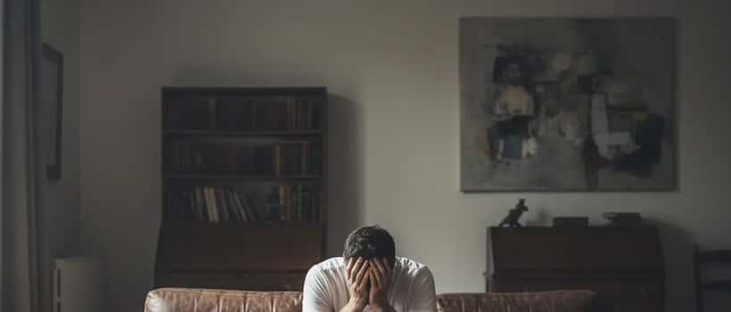 Man sitting alone on sofa head in hands representing male mental health struggle