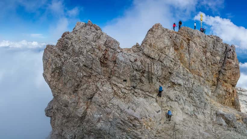 Wanderer auf dem Zugspitze-Gipfel mit Blick auf das Gipfelkreuz bei klarem Herbsthimmel