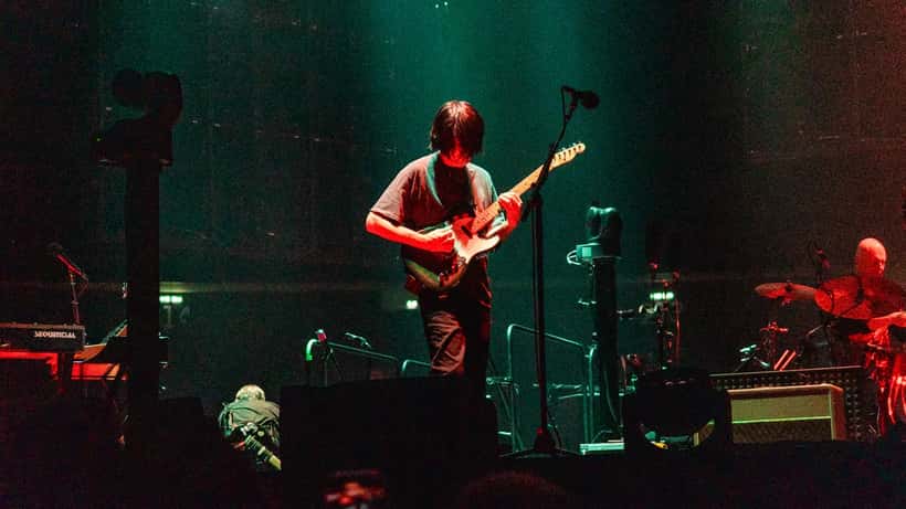 Radiohead performing live at Uber Arena with in-the-round stage setup and bright concert lighting over the crowd