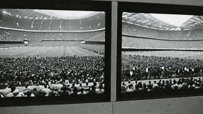 Consulente finanziario italiano guarda Champions League su schermo con documenti di investimento sul tavolo