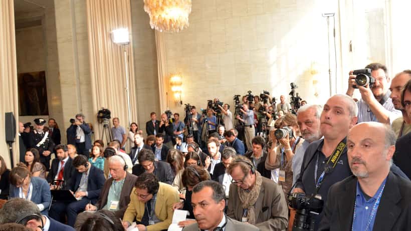 Giornalisti in attesa durante una conferenza stampa con apparecchiature fotografiche e taccuini