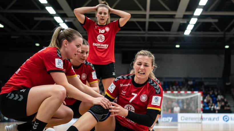 Handballspielerin hält ihr Knie auf dem Spielfeld nach einer Verletzung beim Landung