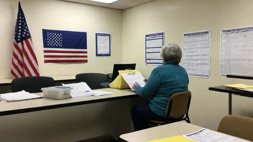 Woman filling out voter registration forms at a county election office with American flag in background