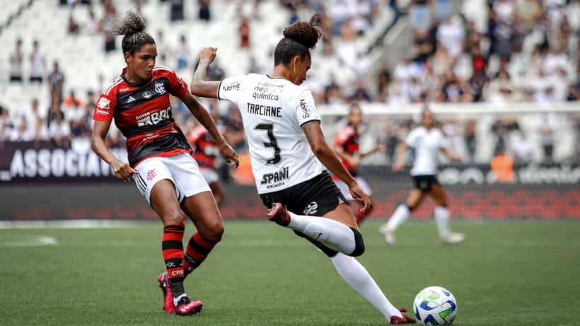 Jogadores de Corinthians e Flamengo em disputa durante a Supercopa, adeptos no estádio ao fundo