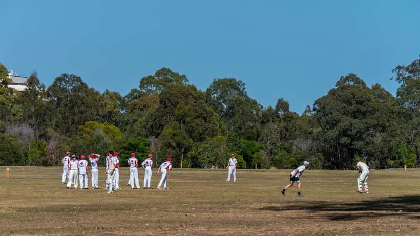 Recreational cricket players on a community park pitch in warm weather
