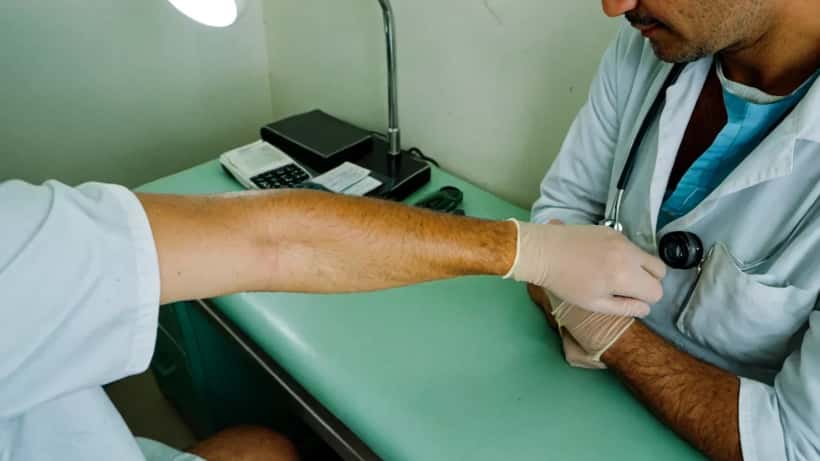 Médico examinando lesões cutâneas de paciente com mpox em clínica brasileira, usando luvas e equipamento de proteção