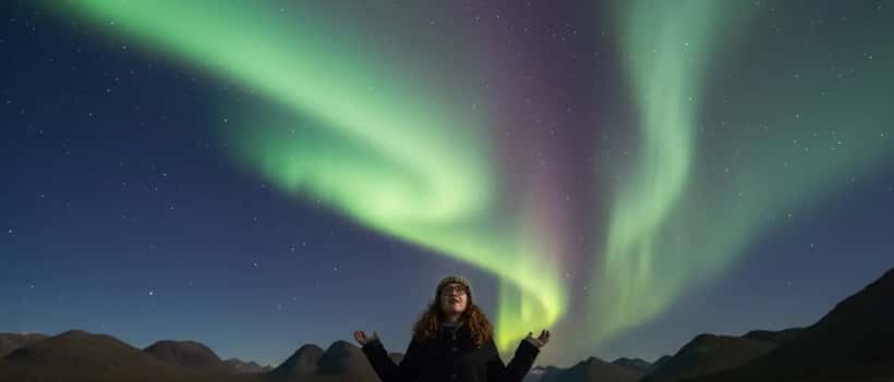 Person in glasses looking up at green and purple aurora borealis in a Scottish night sky