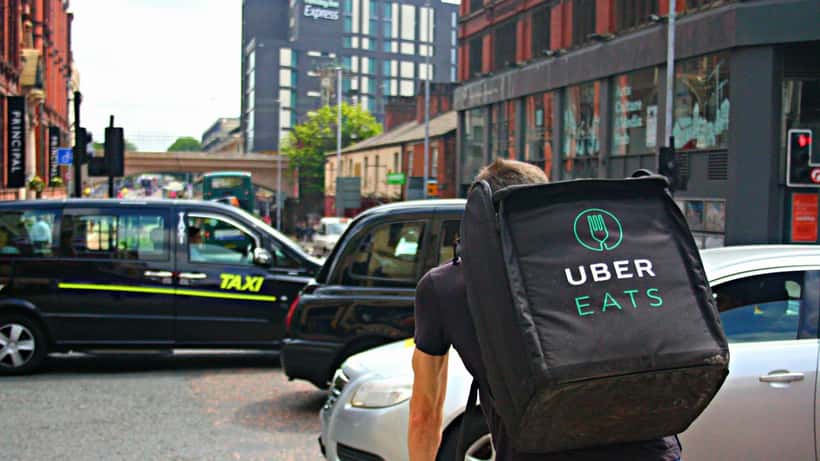Uber Eats-bud cykler gennem travl bygate med leveringspose