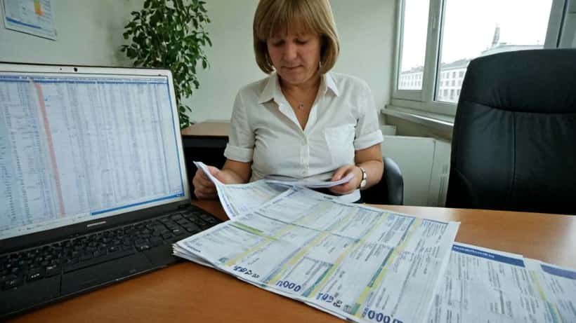 Deutsche Frau im Büro hält Lohnabrechnung mit 1000 Euro Bonus in der Hand, Euroscheine auf dem Schreibtisch