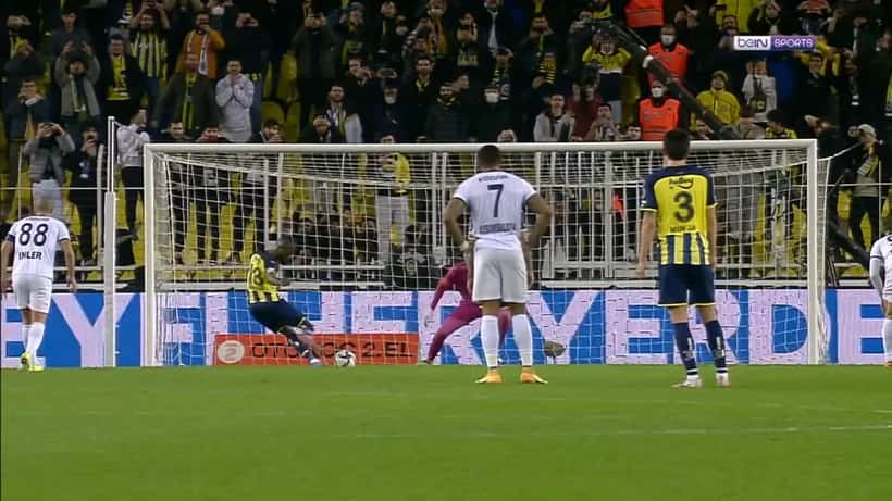 Atleta a bater um pênalti em jogo de futebol com adeptos no fundo