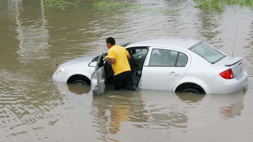 Résident poussant une voiture dans les eaux de crue lors d'un ouragan
