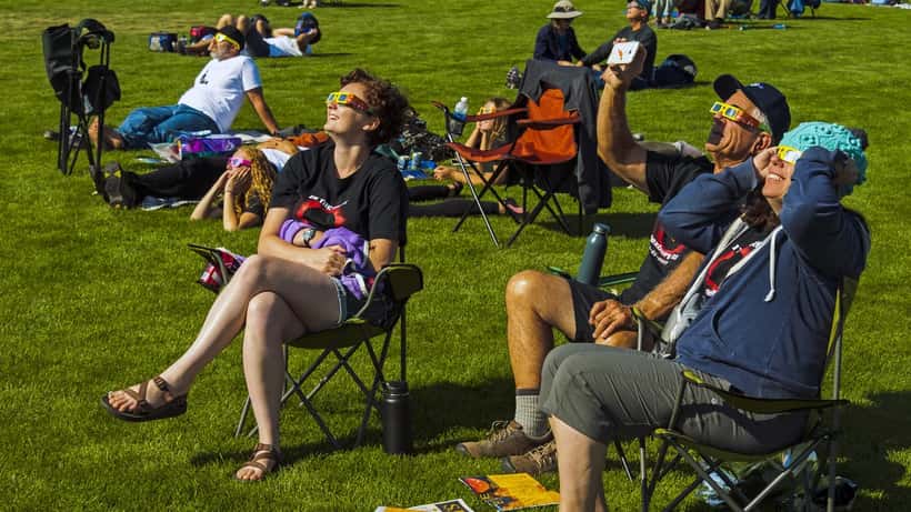 Mensen kijken met eclipsbrillen naar een gedeeltelijke zonsverduistering in een park