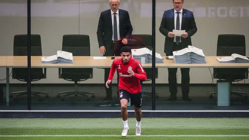 Junger Bundesliga-Spieler im Training mit Vertragsunterlagen im Hintergrund