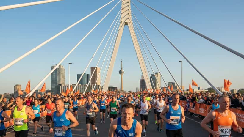 Hardlopers steken de Erasmusbrug over tijdens de 45e NN Marathon Rotterdam in april 2026, met een loper die zijn knie vasthoudt op de voorgrond