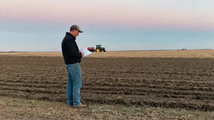 Prairie farmer reviewing financial documents in a spring field at dawn, facing tariff-driven financial pressure in 2026 planting season