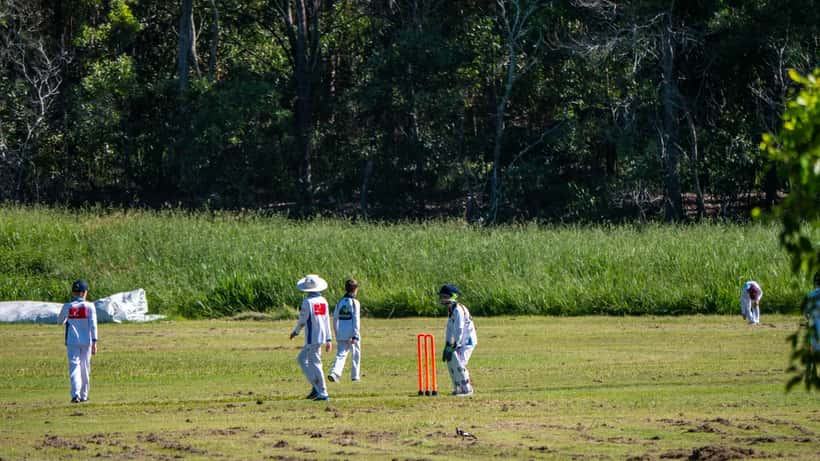 Cricket match in progress at a suburban Australian oval, batsman and wicketkeeper at the crease