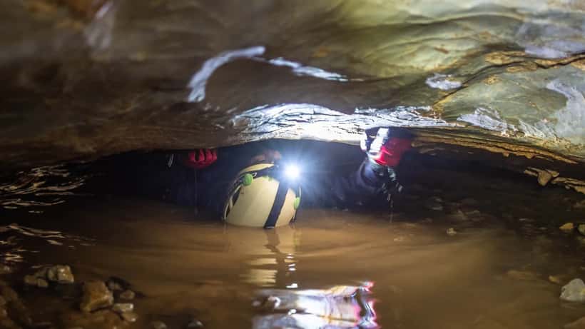 Speleologo in tuta da speleologia che striscia attraverso una stretta galleria sotterranea