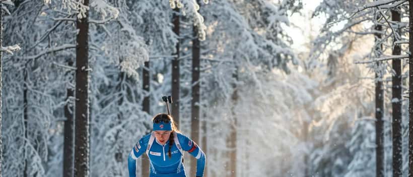 Femme athlète de ski de fond en forêt hivernale enneigée avec équipement de biathlon