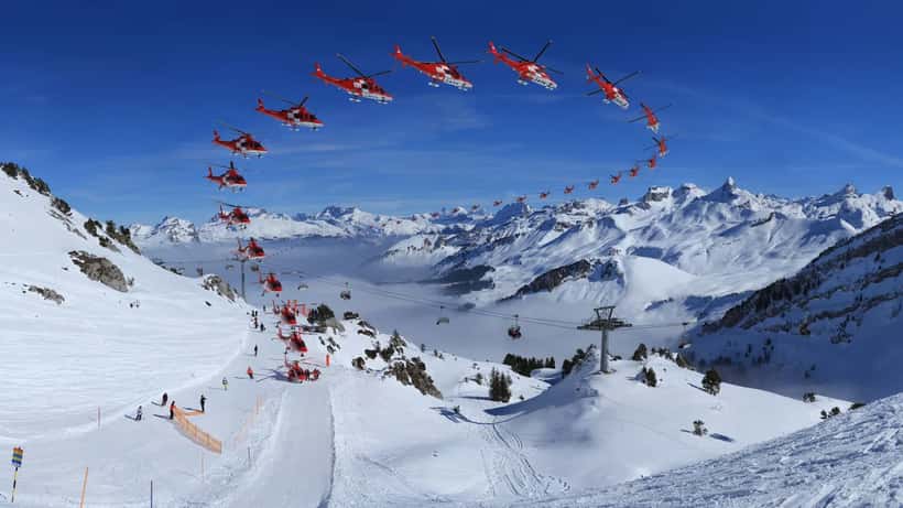 Hélicoptère de secours REGA survolant les Alpes, mission hélitreuillage en montagne
