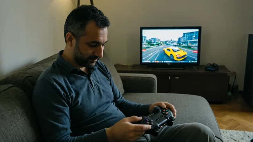 Uomo italiano in salotto con controller da gioco e laptop aperto su impostazioni di sicurezza