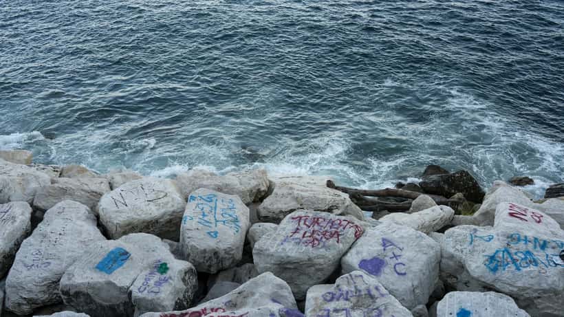 Vista del mare di Napoli con rocce costiere in primo piano e cielo drammatico