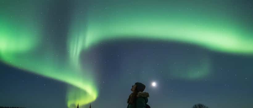 Person beobachtet grüne Polarlichter im nächtlichen Himmel über einer deutschen Landschaft, warme Winterkleidung