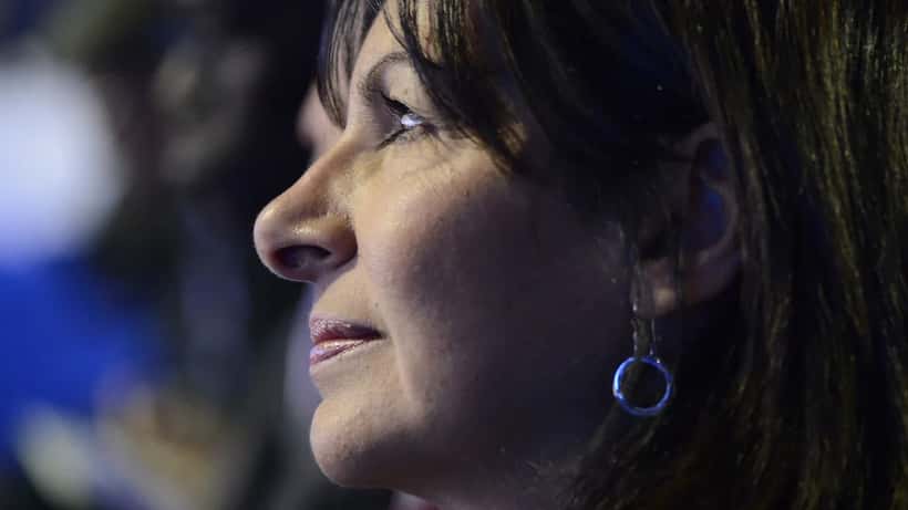 Femme politique à un pupitre devant une mairie, foule en arrière-plan