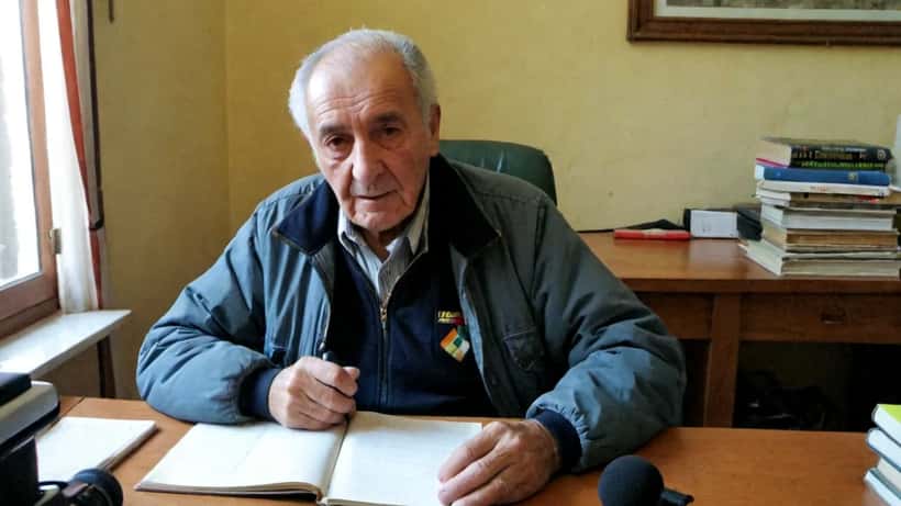 Uomo anziano italiano che parla con determinazione davanti a un microfono, stile fotoreportage documentario