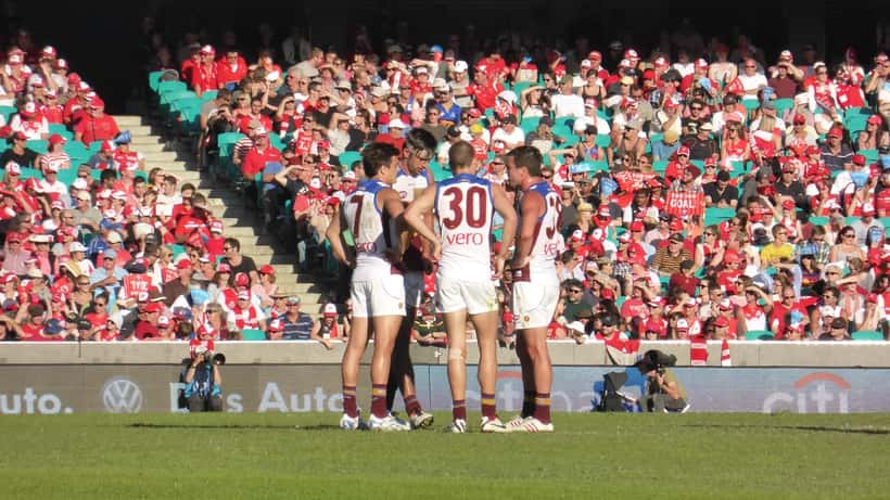 Brisbane Lions AFL players in gold and maroon uniforms on the field