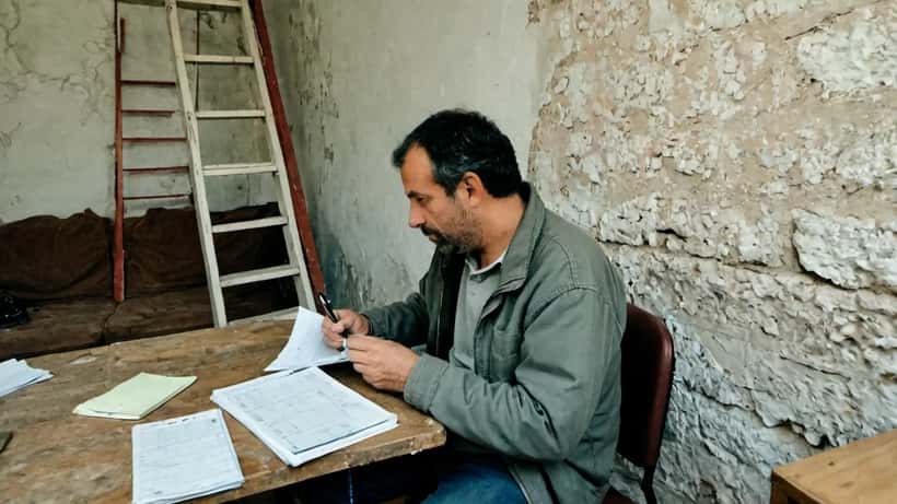 Propriétaire français examinant un devis de travaux avec un regard suspicieux dans une maison en rénovation