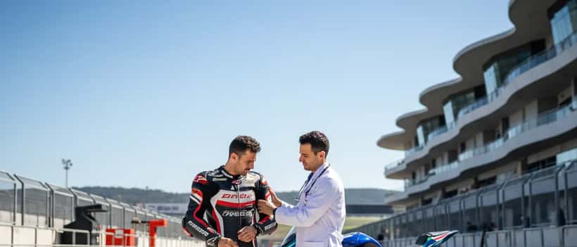 Piloto de motociclismo português sendo examinado por médico desportivo no paddock do Autódromo de Portimão, moto BMW ao fundo