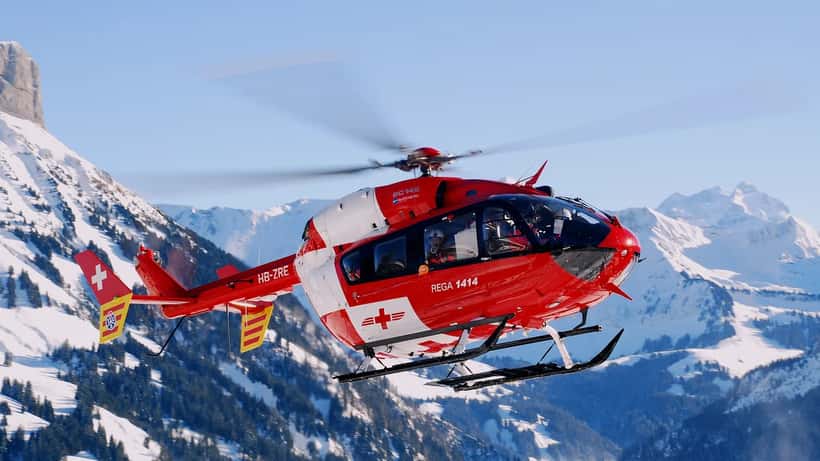 Hélicoptère de la Rega survolant les Alpes suisses lors d'une mission de sauvetage en montagne