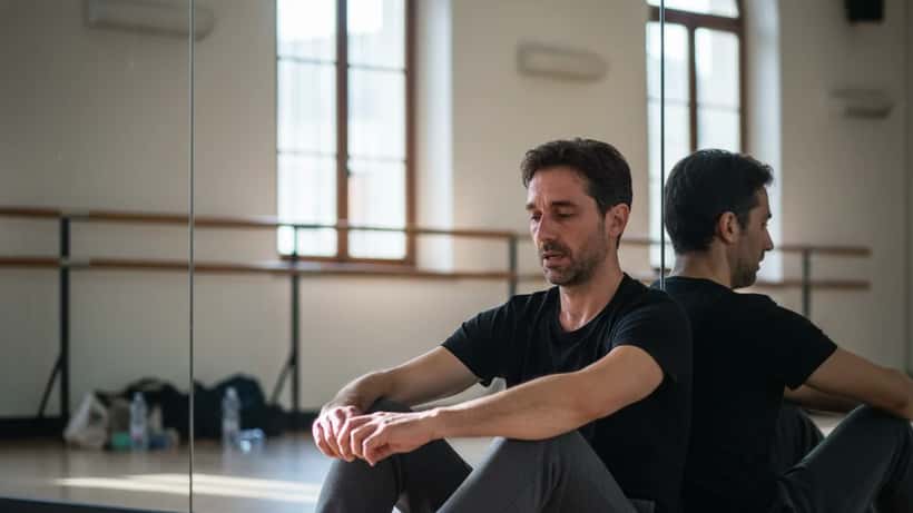 Ballerino professionista affaticato seduto in sala prove con espressione riflessiva