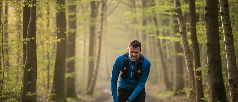 Un coureur de trail en forêt tenant son genou, blessure typique en trail running