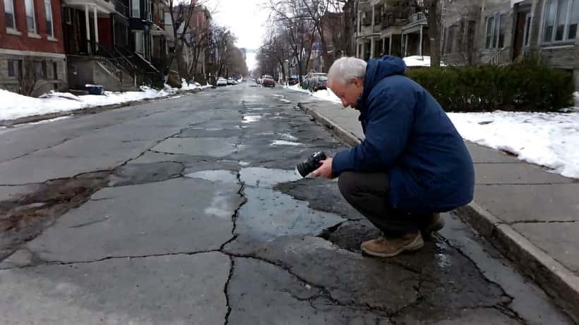 Propriétaire inspectant un trottoir fissuré devant son triplex montréalais au printemps
