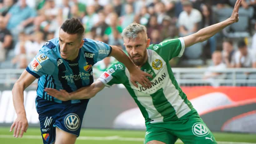 Hammarby och Djurgårdens spelare i närkamp under Stockholmsderbyt, publikfylld arena i bakgrunden
