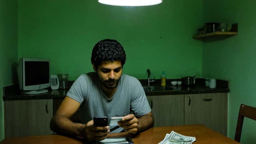 Homem brasileiro consultando o aplicativo FGTS da Caixa no celular em mesa de cozinha em São Paulo
