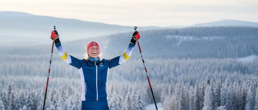 Ung svensk kvinna i skiddräkt på snötäckt skidspår, segerpose, vintrig skog