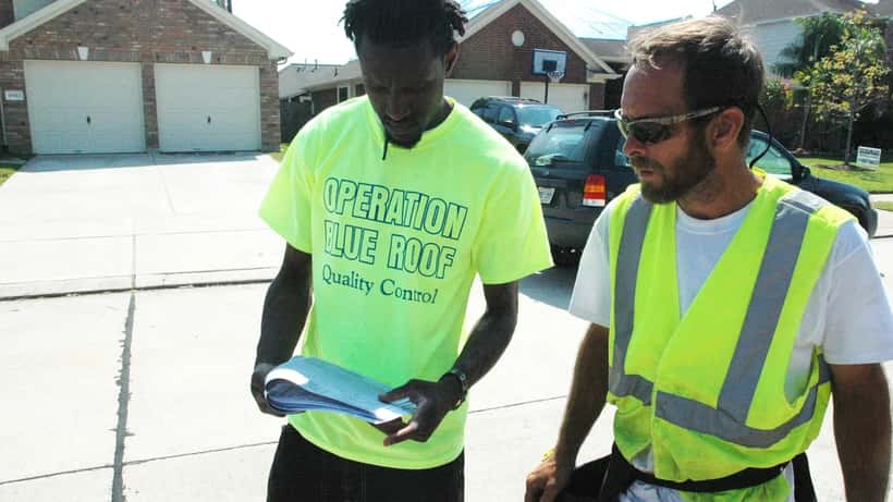 Workers installing temporary blue tarps on a storm-damaged roof following a tornado