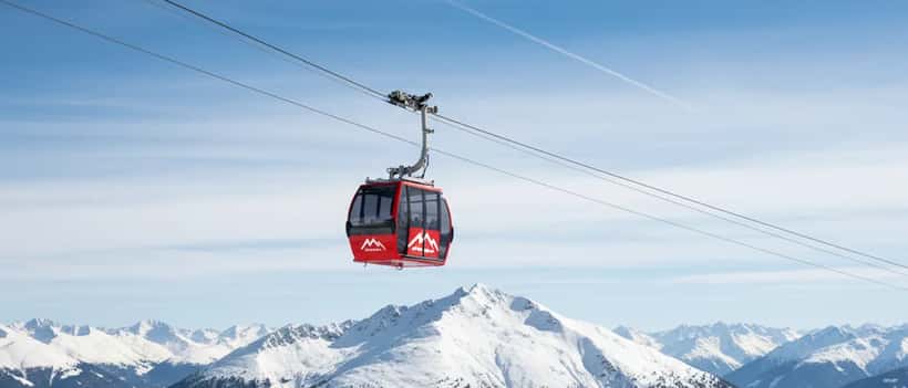 Cabine de teleférico vermelho e branco percorrendo cabo sobre encosta alpina nevada na Suíça com céu azul