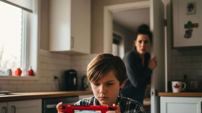 Child playing Nintendo Switch Pokemon game at kitchen table while parent watches